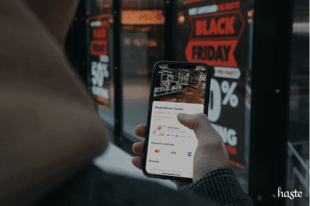 Capa do artigo como criar cupom de desconto no WooCommerce, em que uma pessoa está segurando o celular na frente de uma loja com um banner sobre a black friday.